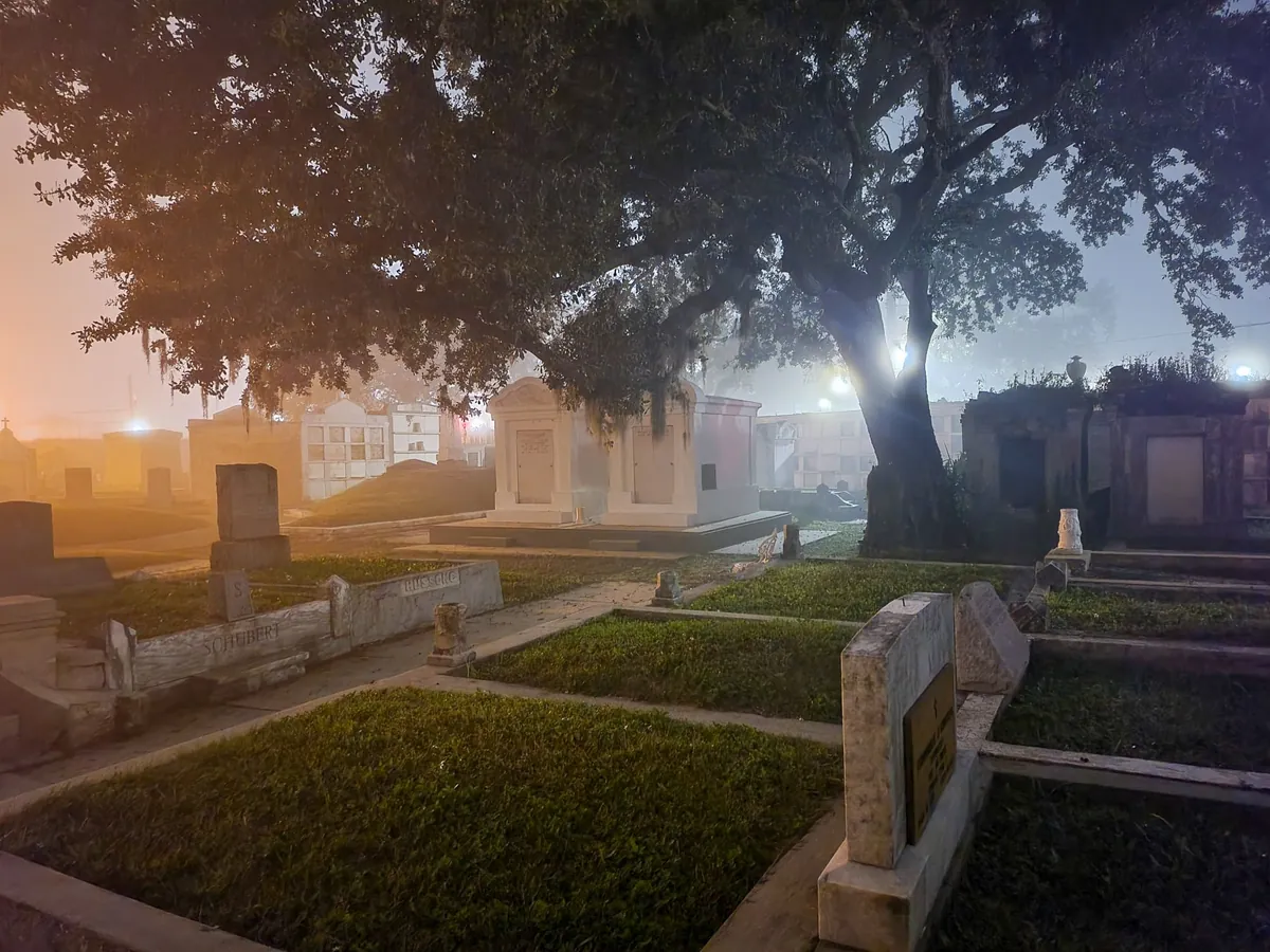 Above-ground tombs under a live oak hung with Spanish moss, lit by lamps in heavy fog at night